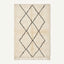 A rectangular cream-colored rug with a black diamond lattice pattern and fringe along the bottom edge, shown against a plain off-white background.