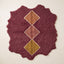 Burgundy Beni Ourain rug with stacked diamond motifs in camel, dusty rose, and gold with cream outlines on a plain background, irregular wavy edges