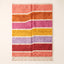 Full flat view of Tamuli Azilal rug with horizontal striped bands in coral, orange, pink, yellow, purple and red separated by ivory stripes
