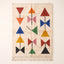 Ivory Azilal rug with coloured triangles and bows in red, orange, navy, pink, green, gold and black, flat lay on plain background