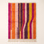 Tanina Azilal rug in magenta, orange, purple, pink and yellow vertical stripes on plain background