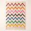 Multicolor Azilal rug with bright zigzag chevron stripes in red, orange, magenta, black, blue, green and gold on an ivory ground, with small black cross accents throughout