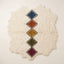 Flat lay of Tafrara Beni Ourain rug with irregular wavy edges, undyed ivory ground and vertical chain of five stacked diamond lozenges in navy, terracotta, gold, olive and burgundy with dark brown and cream outlines