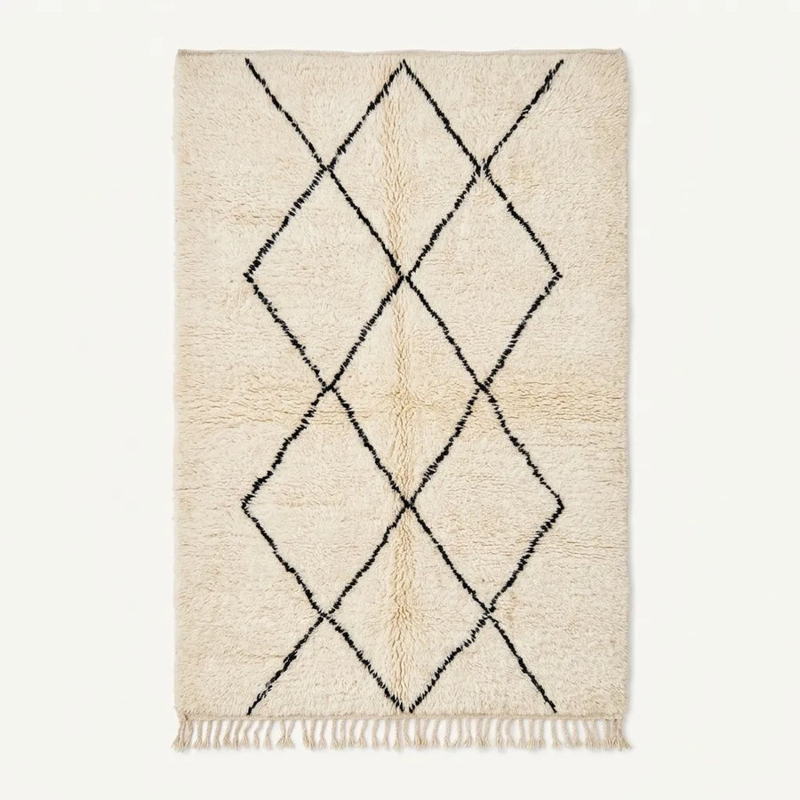 A rectangular cream-colored rug with a black diamond lattice pattern and fringe along the bottom edge, shown against a plain off-white background.