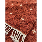 Close-up of the plush terracotta wool texture and ivory cross motifs on the Azru rug.