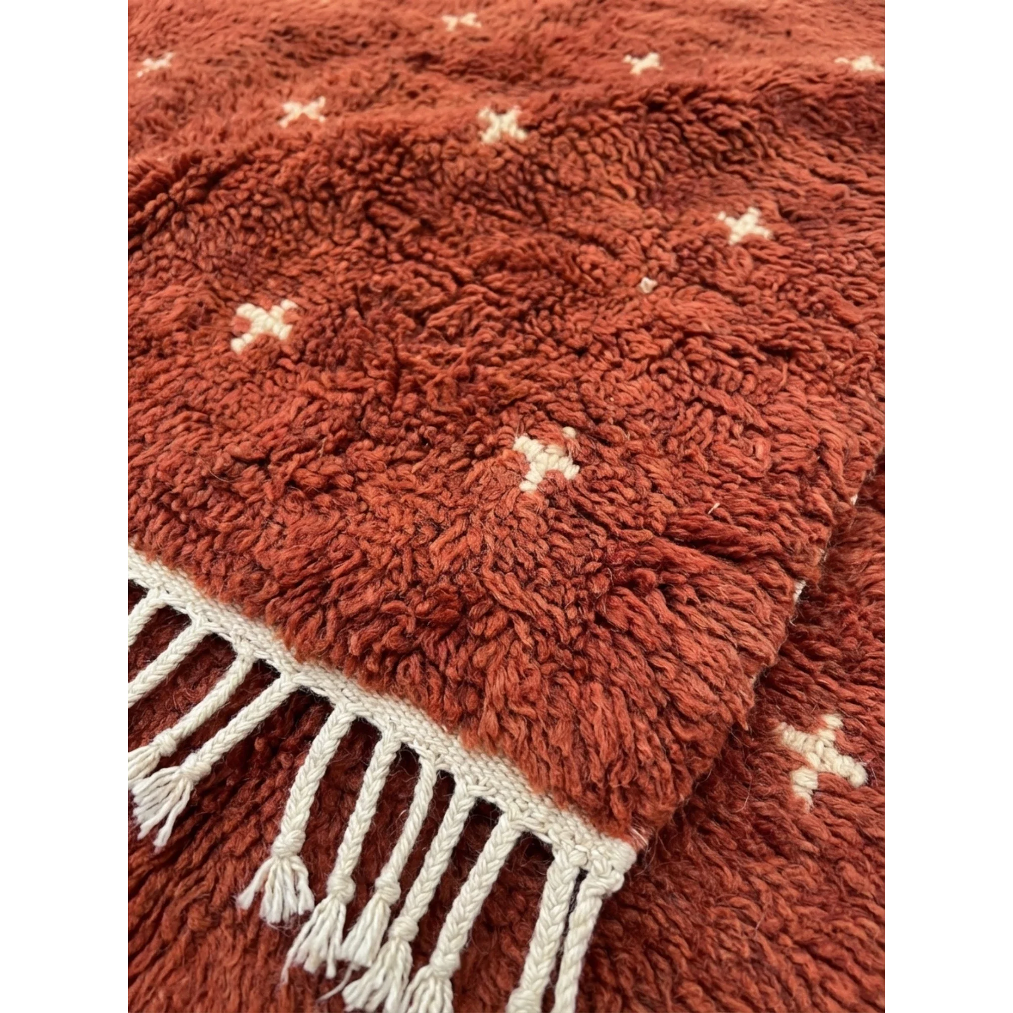 Close-up of the plush terracotta wool texture and ivory cross motifs on the Azru rug.