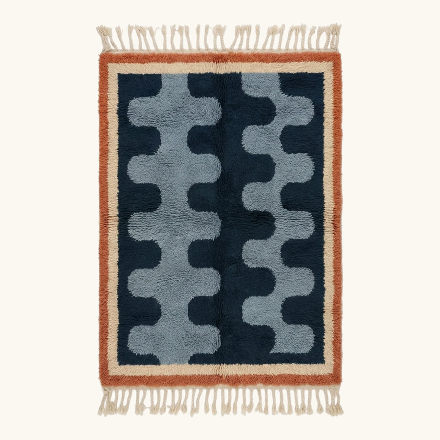 Full view of the Azul Beni Ourain rug with navy and blue abstract pattern, rust border and hand-tied fringe.
