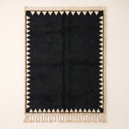 Black and ivory Beni Ourain rug with sawtooth triangle border, flat lay on plain background