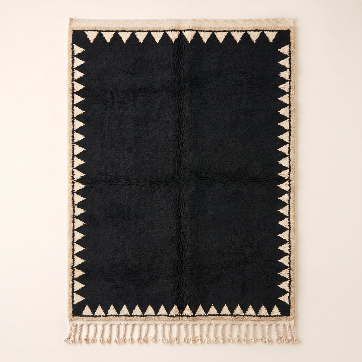 Black and ivory Beni Ourain rug with sawtooth triangle border, flat lay on plain background