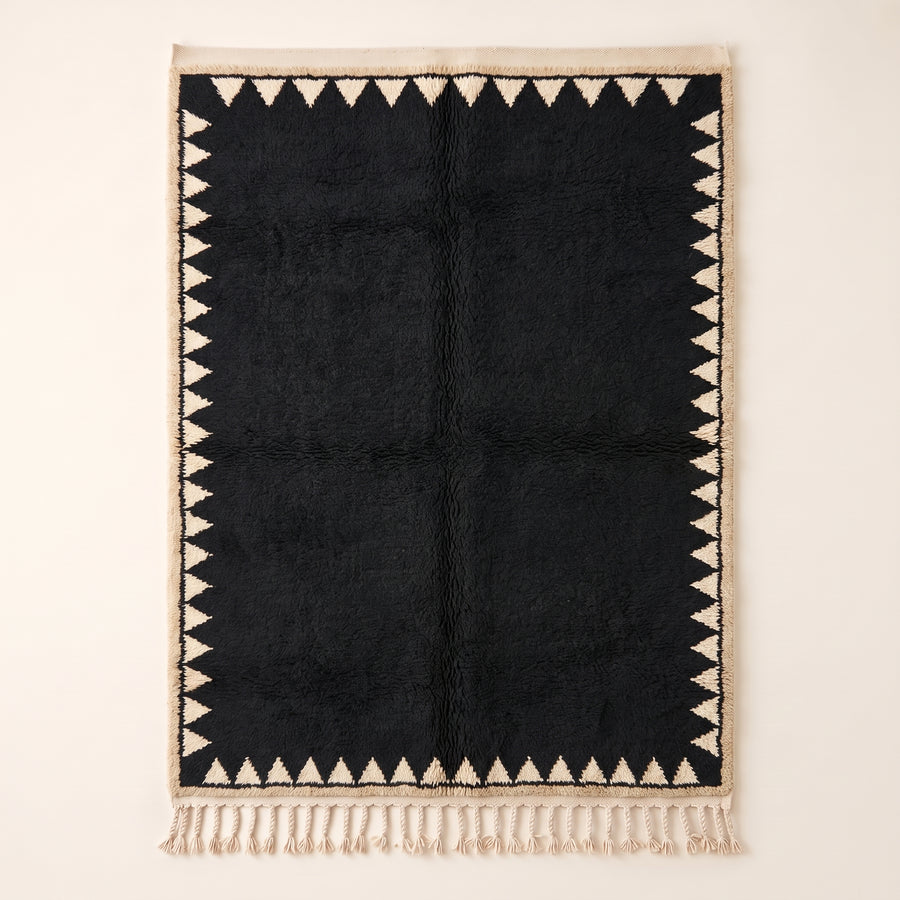 Black and ivory Beni Ourain rug with sawtooth triangle border, flat lay on plain background