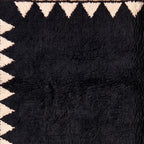 Texture close-up of black wool pile with ivory sawtooth border triangles showing hand-knotted detail