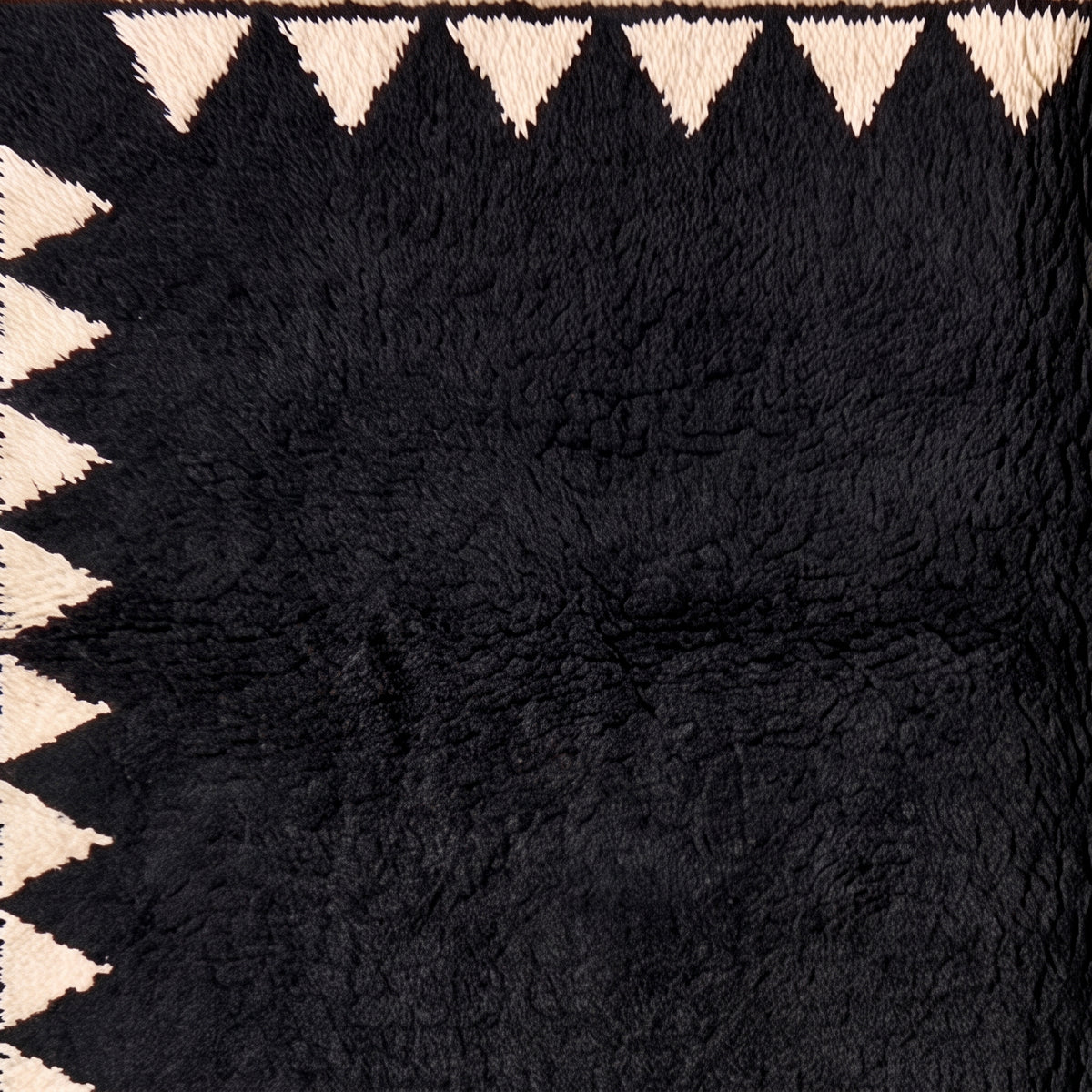 Texture close-up of black wool pile with ivory sawtooth border triangles showing hand-knotted detail