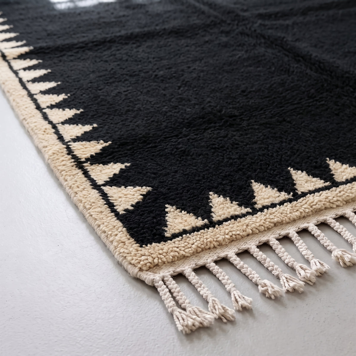 Corner detail showing sawtooth triangle motif and cream wool fringe on black Beni Ourain rug