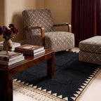 Black Beni Ourain rug with sawtooth border in living room setting with wooden table, upholstered chair and flowers