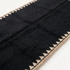 Close-up of thick black wool pile and ivory sawtooth edge detail showing hand-knotted construction