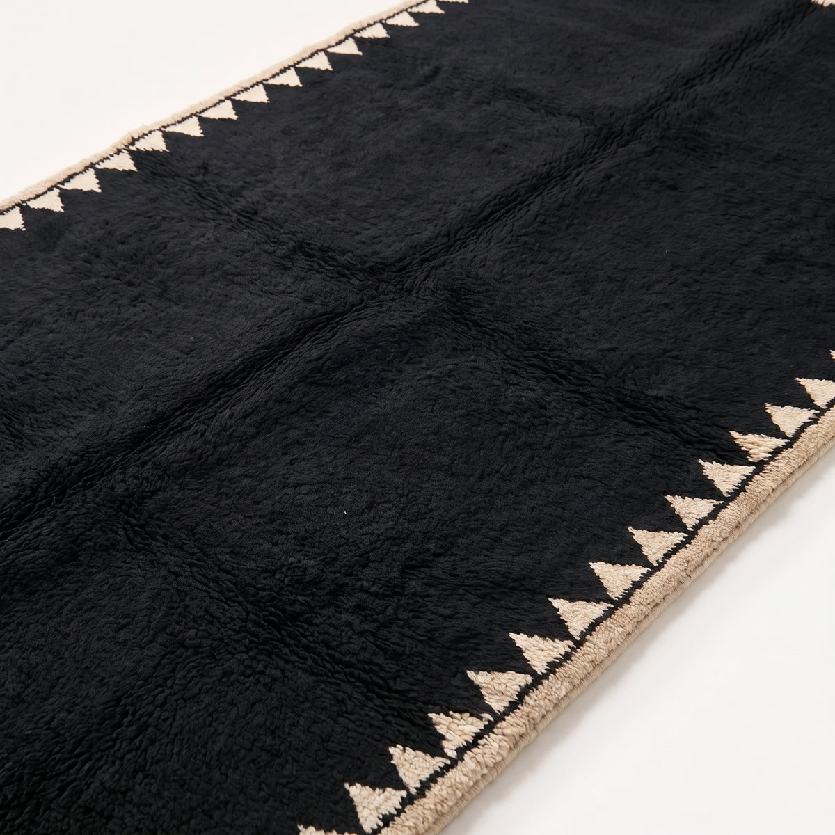 Close-up of thick black wool pile and ivory sawtooth edge detail showing hand-knotted construction