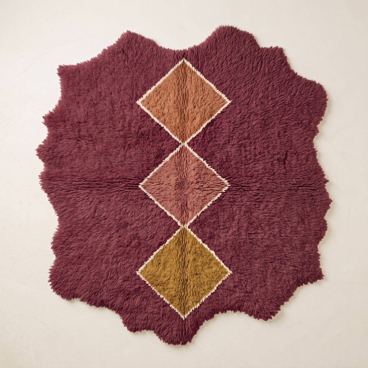 Burgundy Beni Ourain rug with stacked diamond motifs in camel, dusty rose, and gold with cream outlines on a plain background, irregular wavy edges