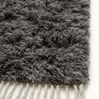 Close-up of charcoal Beni Ourain pile texture showing soft wool knots and ivory fringe edge