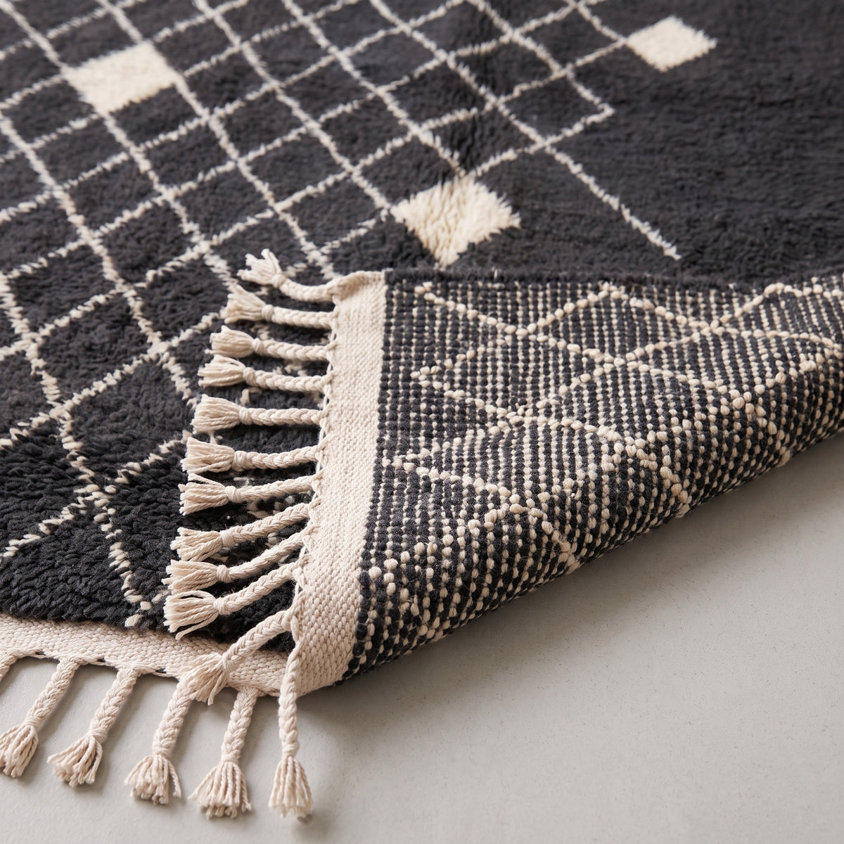 Corner detail of the charcoal and ivory rug showing the diamond motifs and fringe with woven foundation visible