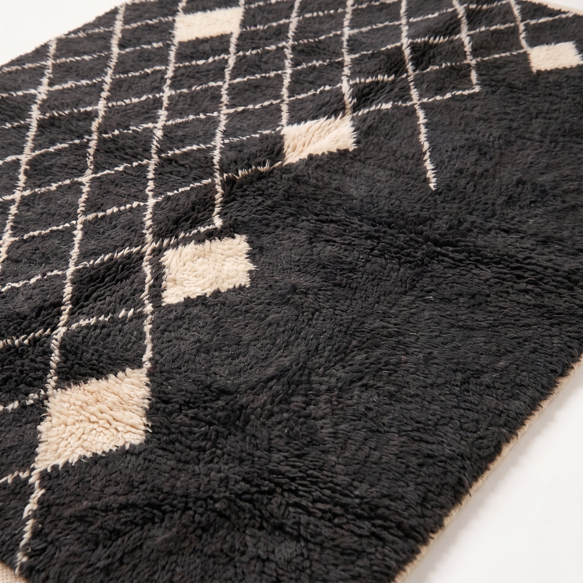 Close-up of the thick, soft wool pile showing the diamond lattice lines and texture of the charcoal and ivory rug