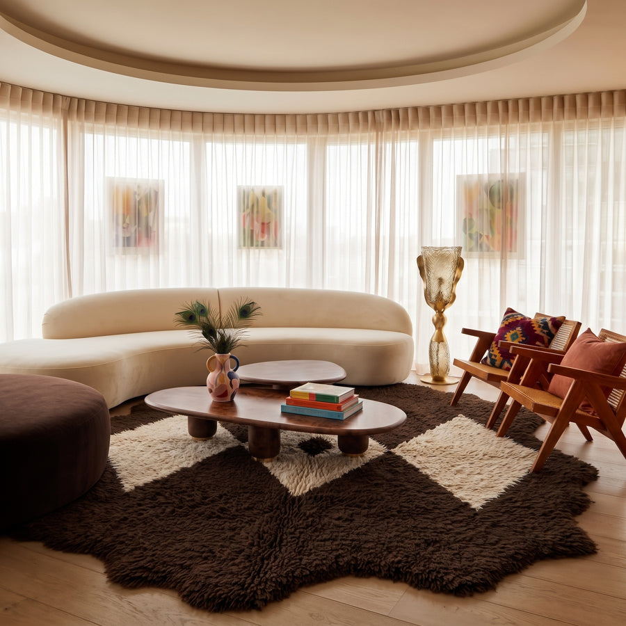 Massa rug in a modern living room with curved cream sofa, dark ottoman, and wood furniture, diamond pattern centred on oval coffee table