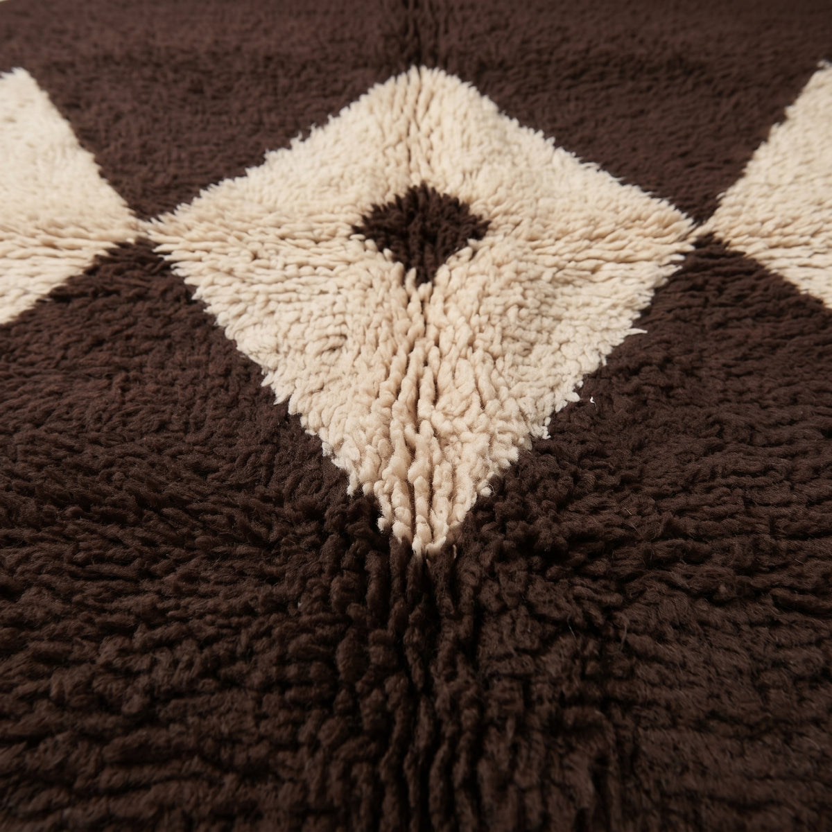 Close-up of Massa's diamond lattice motif showing thick hand-knotted wool pile in chocolate brown and ivory with black centre eye detail