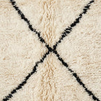 Close-up of a shaggy cream rug with a black woven X pattern crossing at the center.