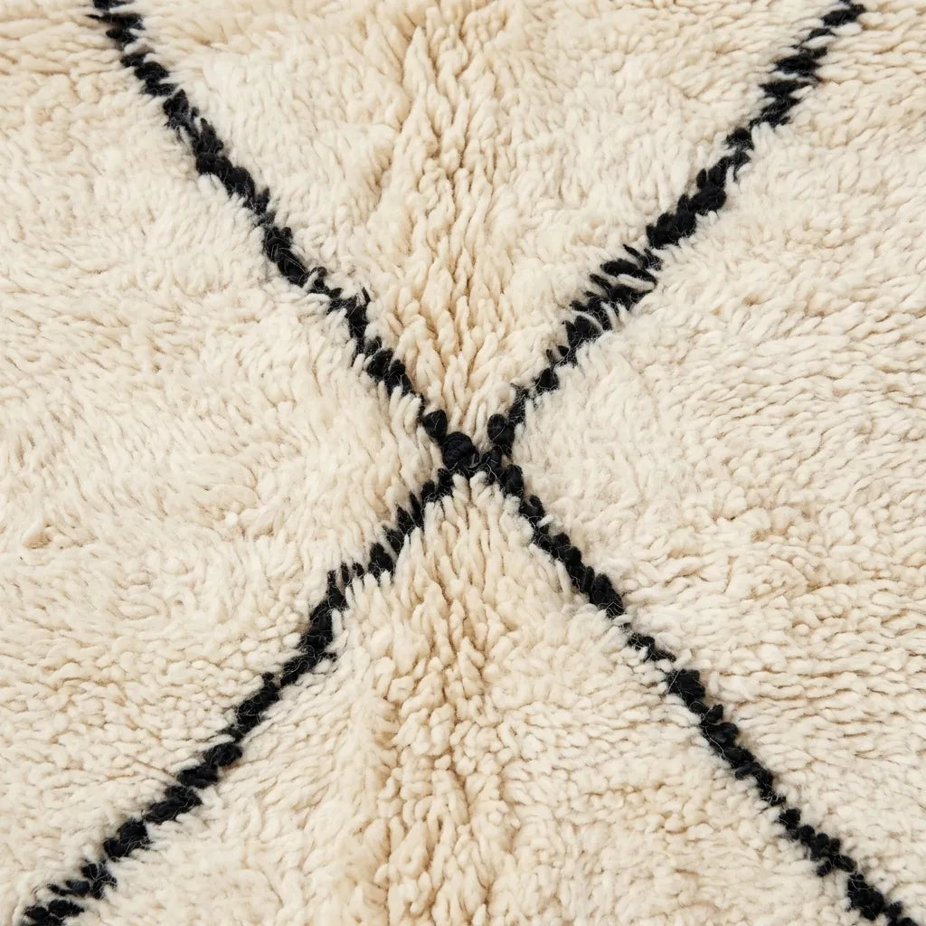 Close-up of a shaggy cream rug with a black woven X pattern crossing at the center.