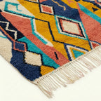 Detailed view of Izuran showing teal, coral, mustard and navy geometric bands beside the rug fringe