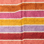 Corner detail of Tamuli rug showing cream fringe and edge of striped bands in coral, orange, pink, yellow, purple and red