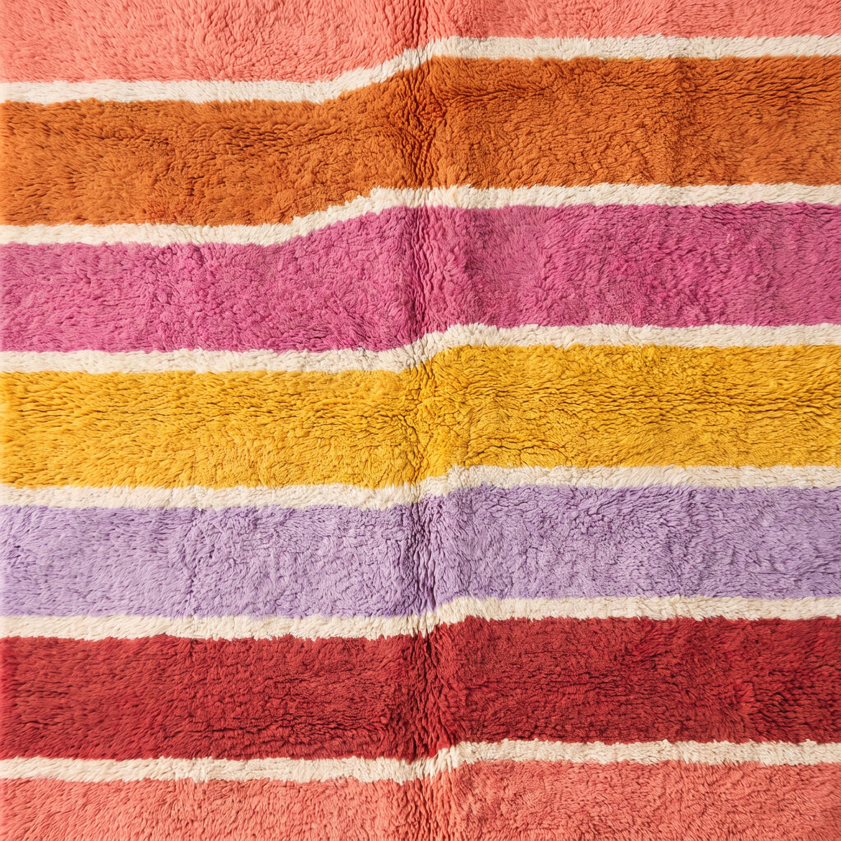 Corner detail of Tamuli rug showing cream fringe and edge of striped bands in coral, orange, pink, yellow, purple and red