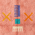 Close-up showing central motif cluster with purple striped rectangle, gold X marks, turquoise square and cream fringe on coral pile