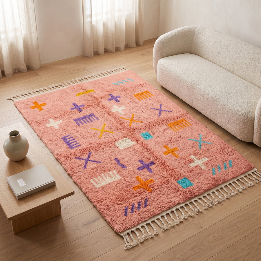 Coral Azilal script rug laid in living room next to cream sofa and side table with vase