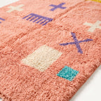 Close-up of plush wool pile showing purple cross and cream block symbols on coral ground