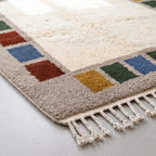 Corner detail showing colour block arrangement and fringe, rust and mustard squares on grey border