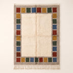 Cream Mrirt rug with colour block border frame in rust, mustard, forest green and slate blue stacked squares, flat lay on plain background