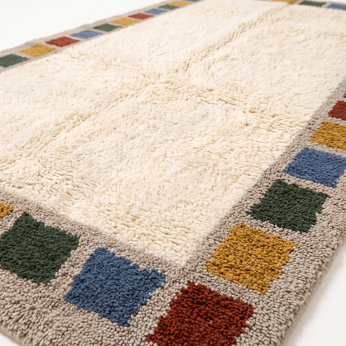 Close-up of plush wool pile showing cream field and dyed colour block borders in rust, mustard, green and blue