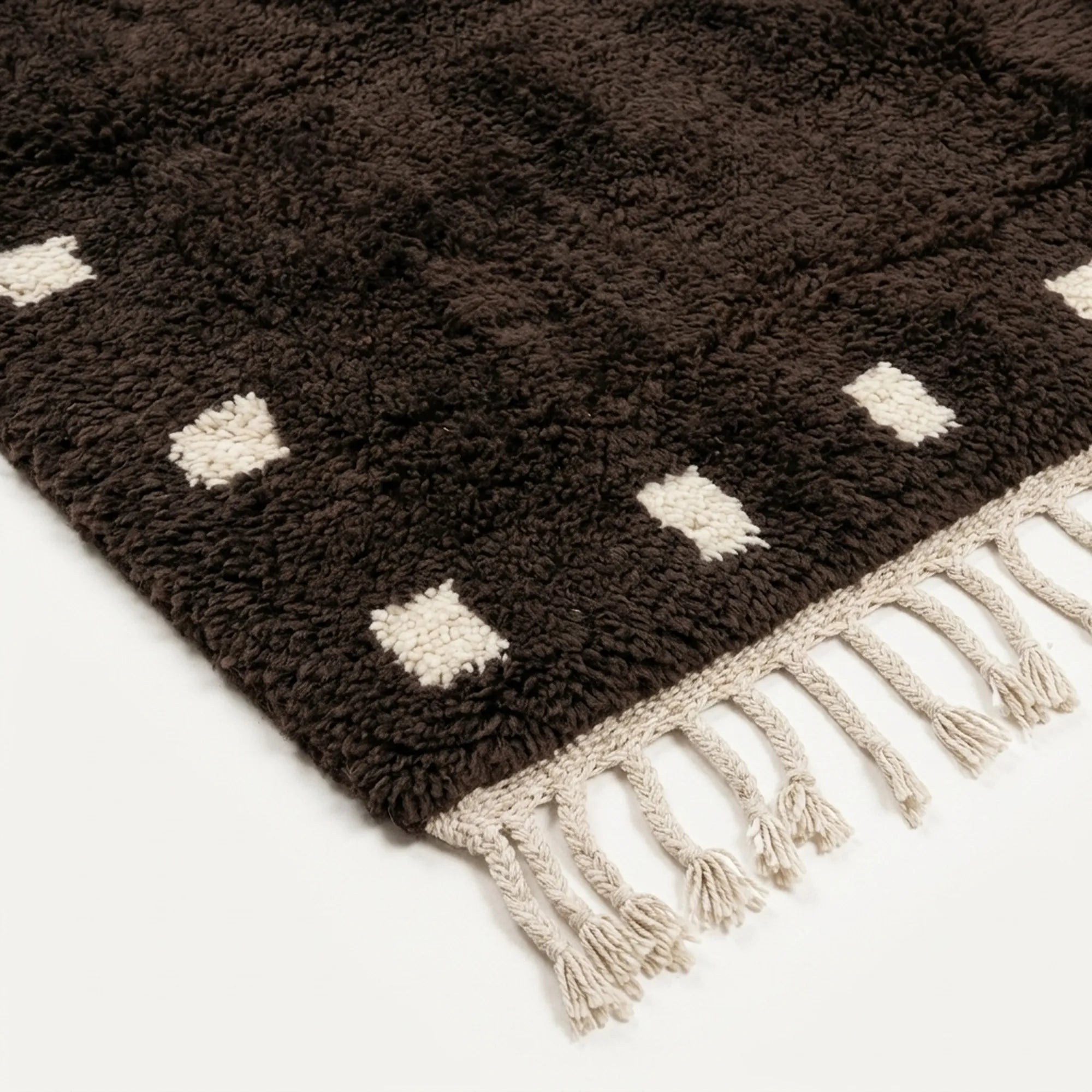 Handmade texture and edge detail of the dark brown and ivory wool rug.