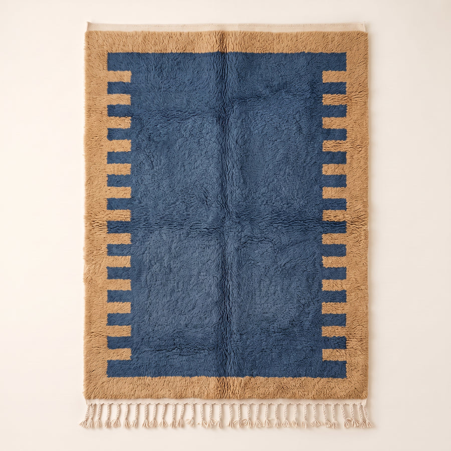 Denim and camel Mrirt rug with comb-edge border motif on plain background, flat lay
