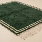 Angled full view of the Tafukt forest green rug showing its ivory double border.