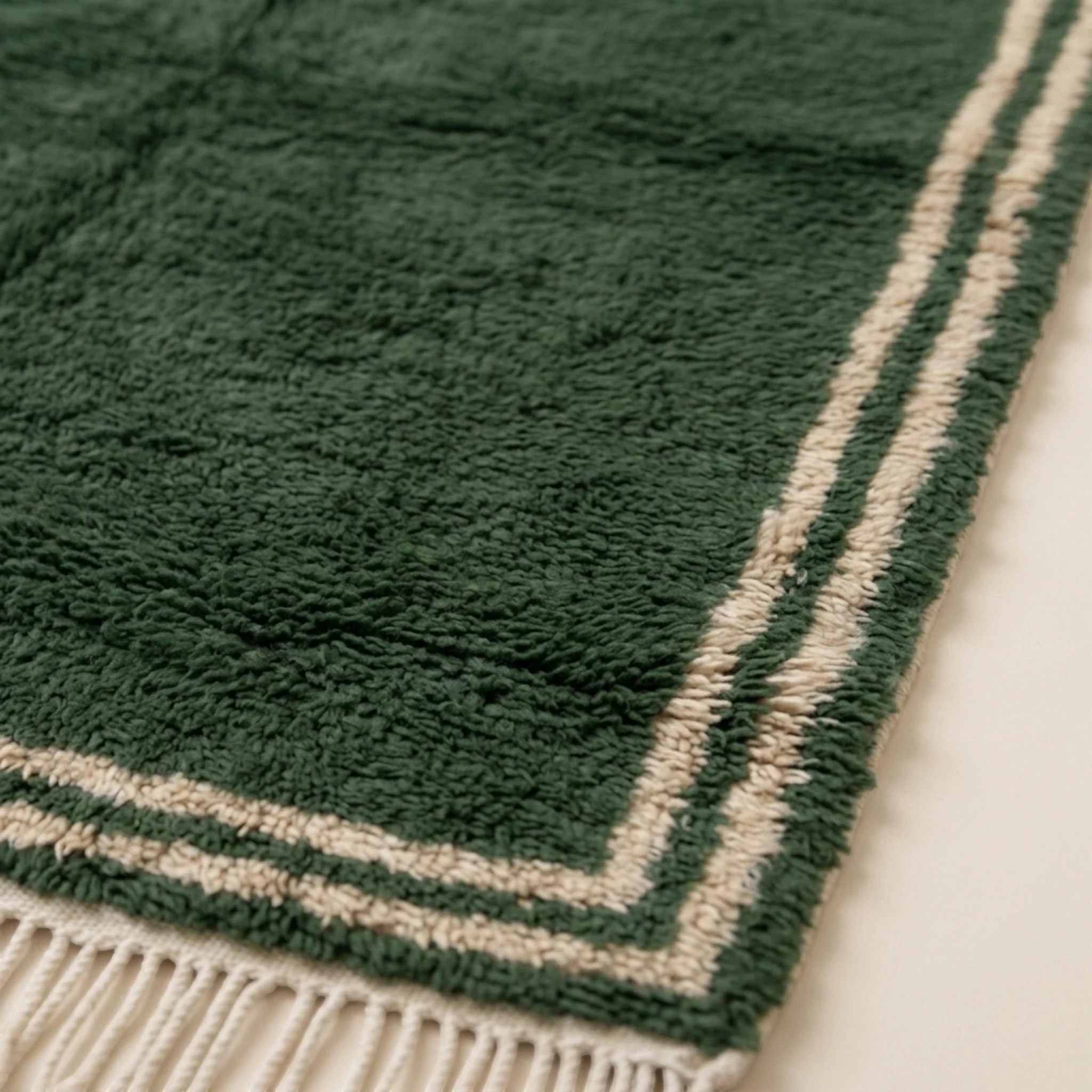 Close view of the ivory double border framing the Tafukt forest green rug.