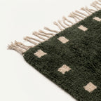 Angled detail of the forest green and ivory hand-knotted wool rug.