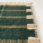 Close-up of the green and ochre horizontal band pattern on the Azru ivory wool rug.