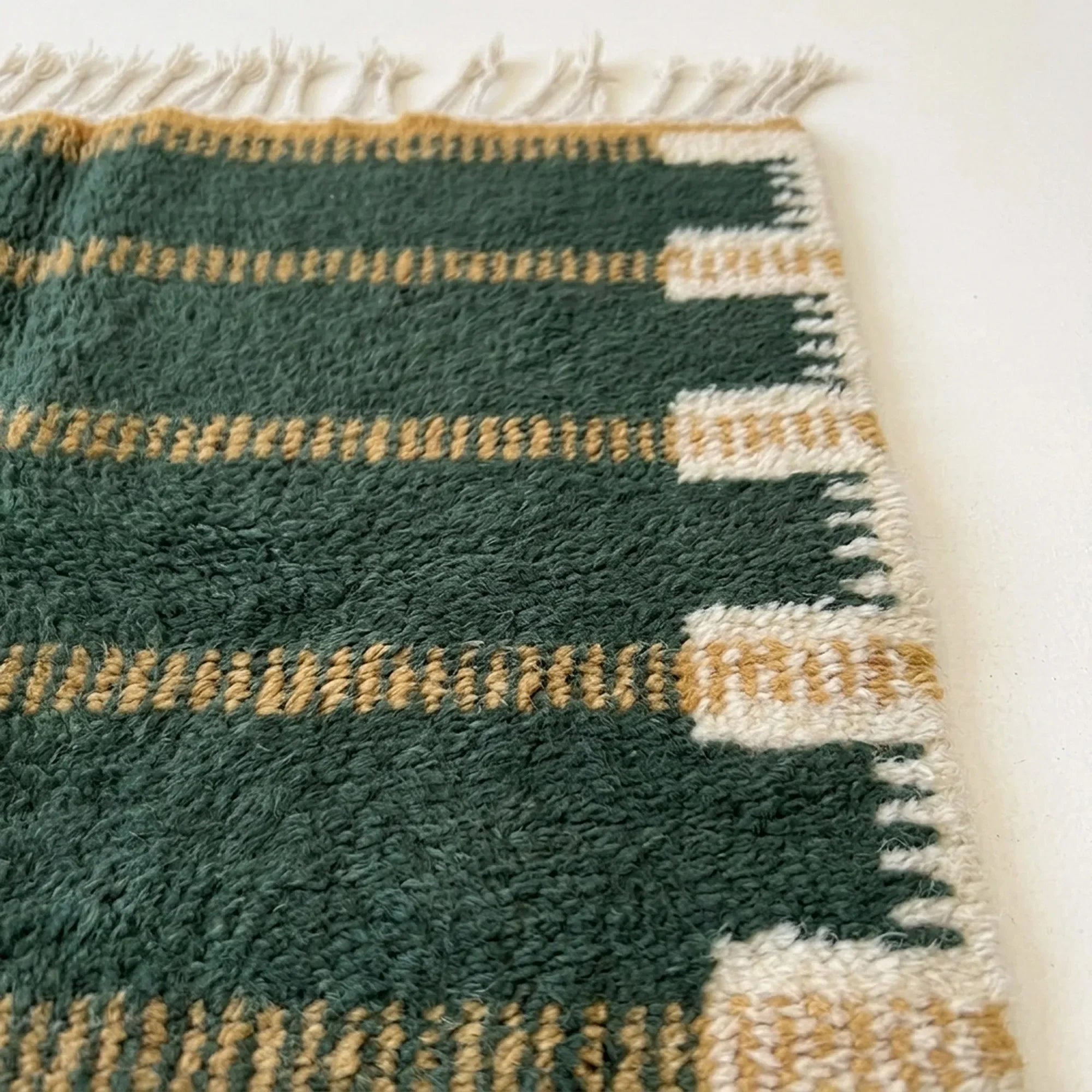 Close-up of the green and ochre horizontal band pattern on the Azru ivory wool rug.