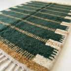 Angled view of the Azru forest green, ochre and ivory hand-knotted Beni Ourain rug.