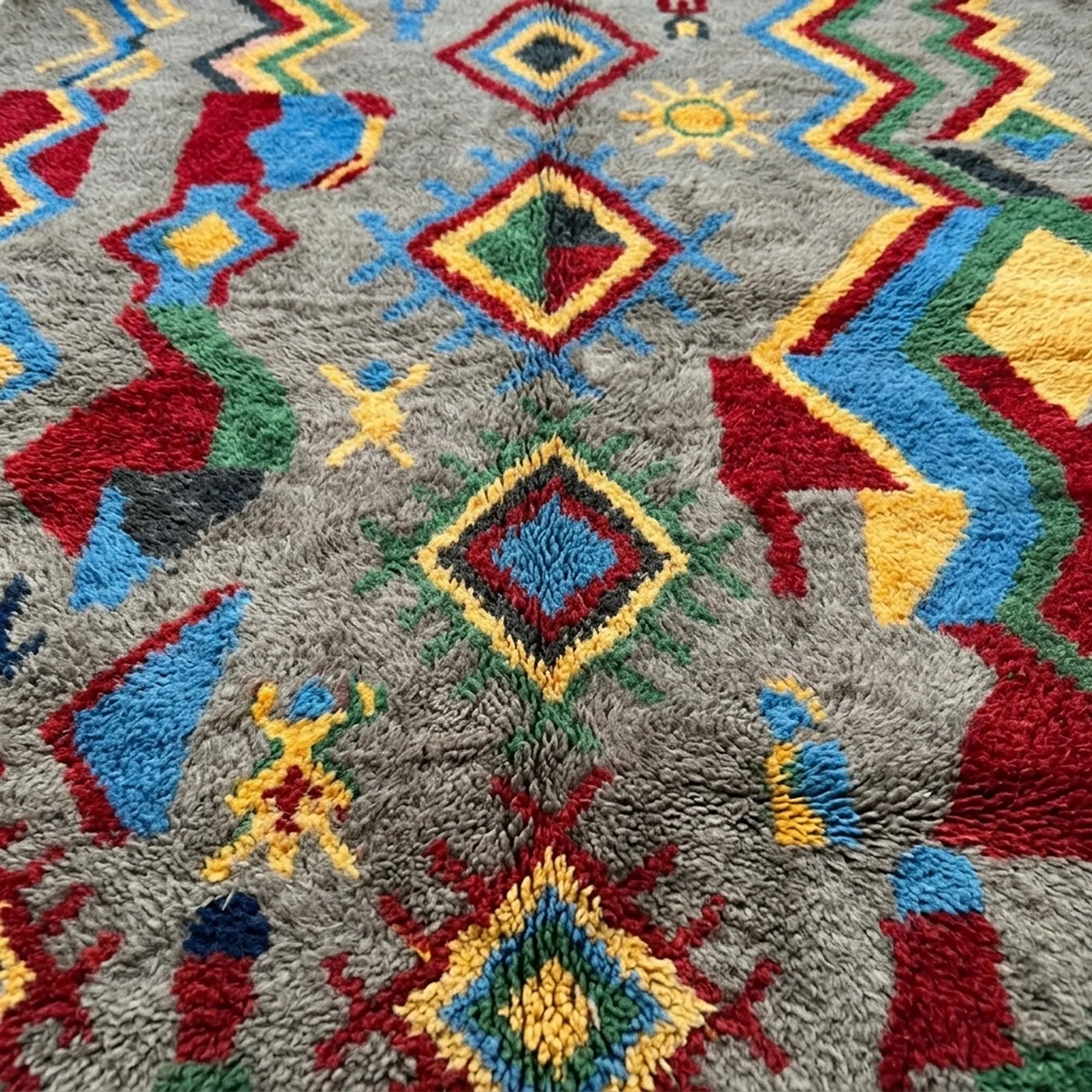 Pattern close-up of Abridan showing colorful diamonds, zigzags and small symbolic marks across the gray wool pile