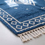 Angled detail of border diamonds and field showing thick soft wool pile in indigo with ivory geometric border