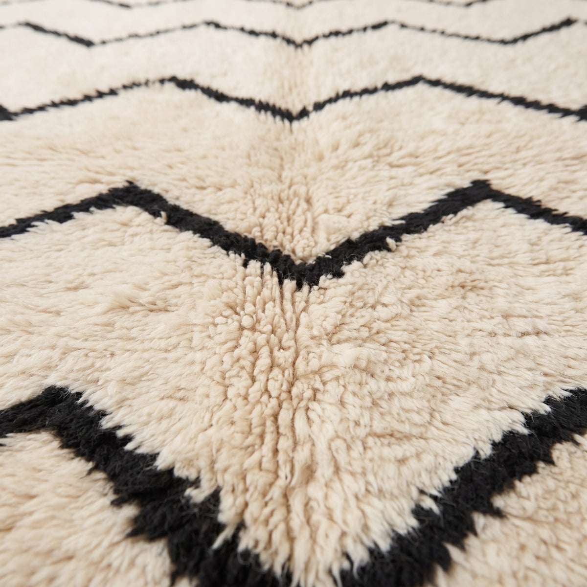 Close-up of thick hand-knotted wool pile showing black chevron stripe detail and soft ivory background