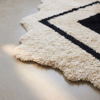 Edge detail showing soft fringed hem and irregular wavy border of ivory and black rug