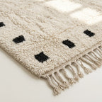 Angled detail of the ivory and black hand-knotted wool rug.